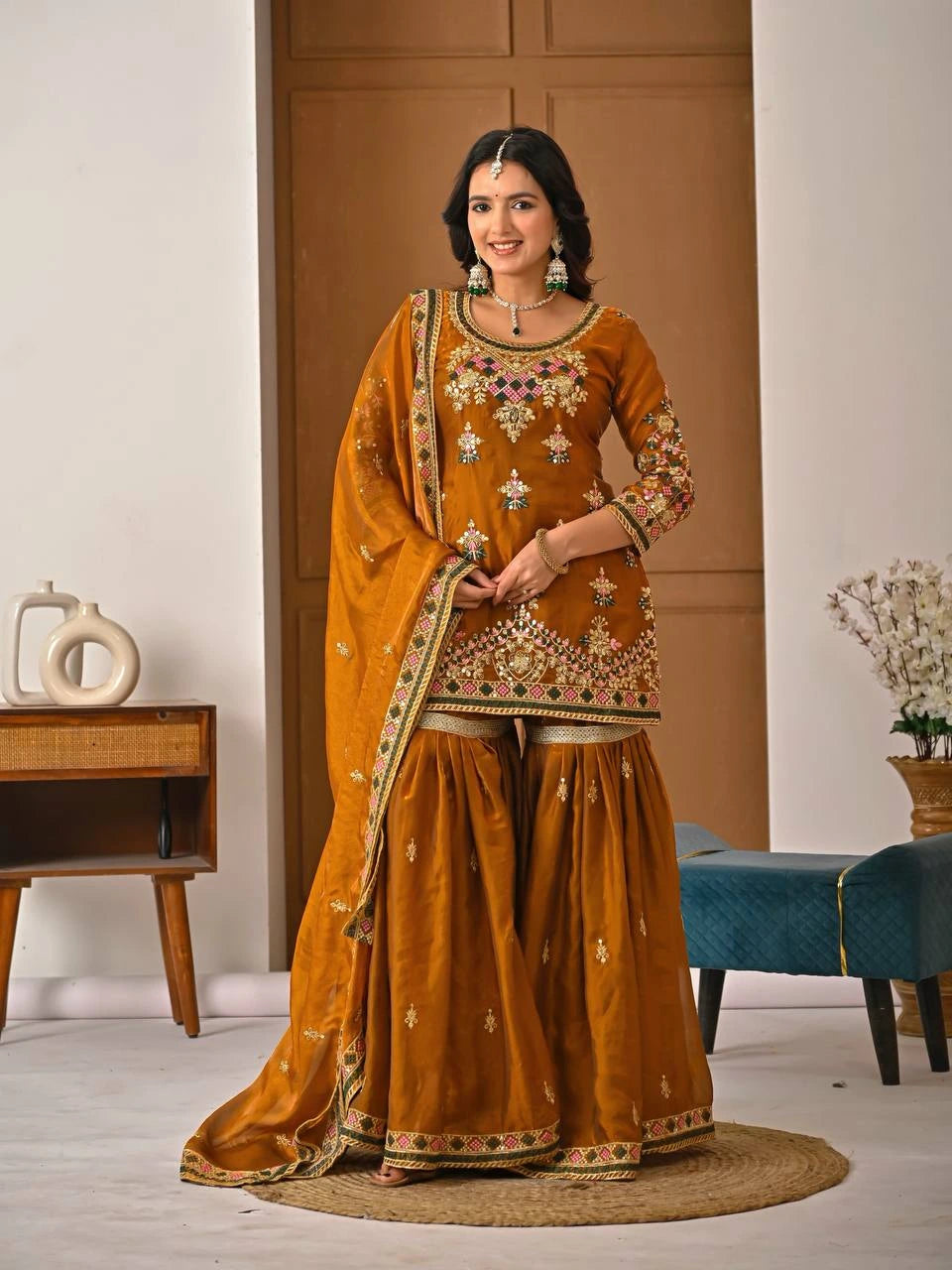 Woman in a traditional mustard yellow outfit with intricate patterns in a room setting.